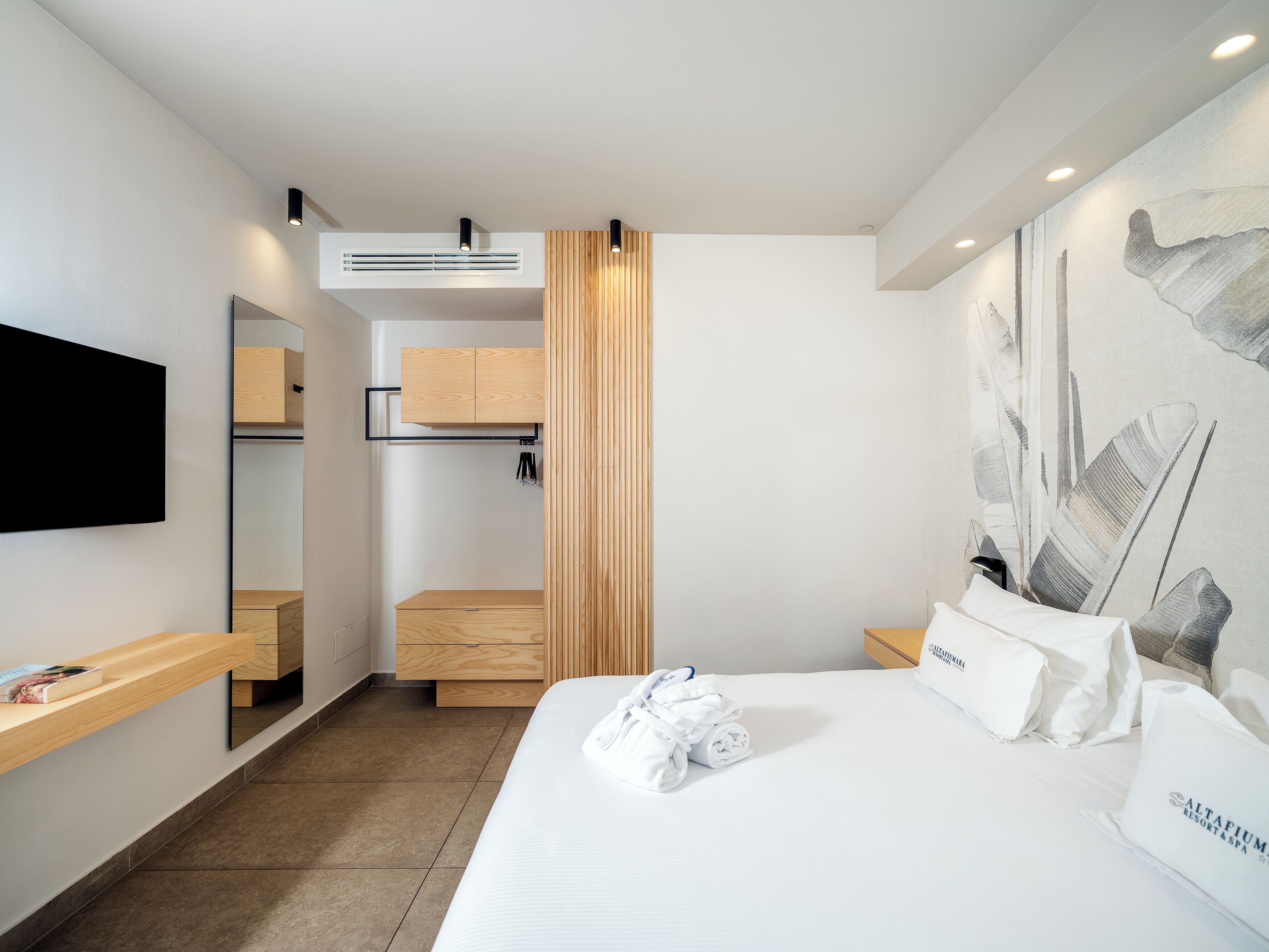 A modern hotel room with a bed, a flat-screen TV, a wooden wardrobe, and a wall-mounted air conditioner.