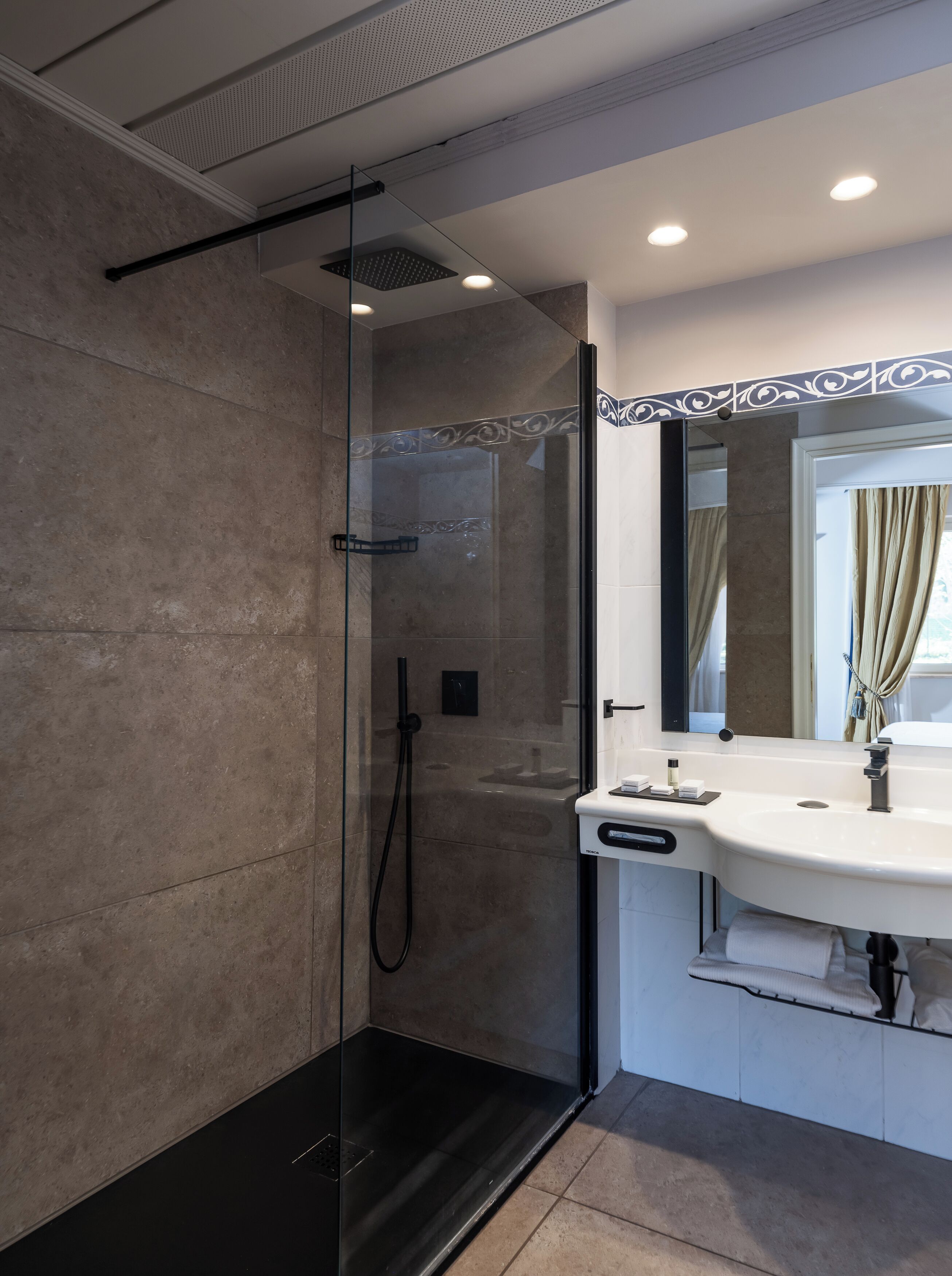 Un baño moderno con ducha envuelta en cristal, un lavabo blanco y un espejo con un marco decorativo.