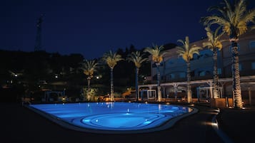 Una piscina con iluminación azul, rodeada de palmeras y un edificio con varios balcones.