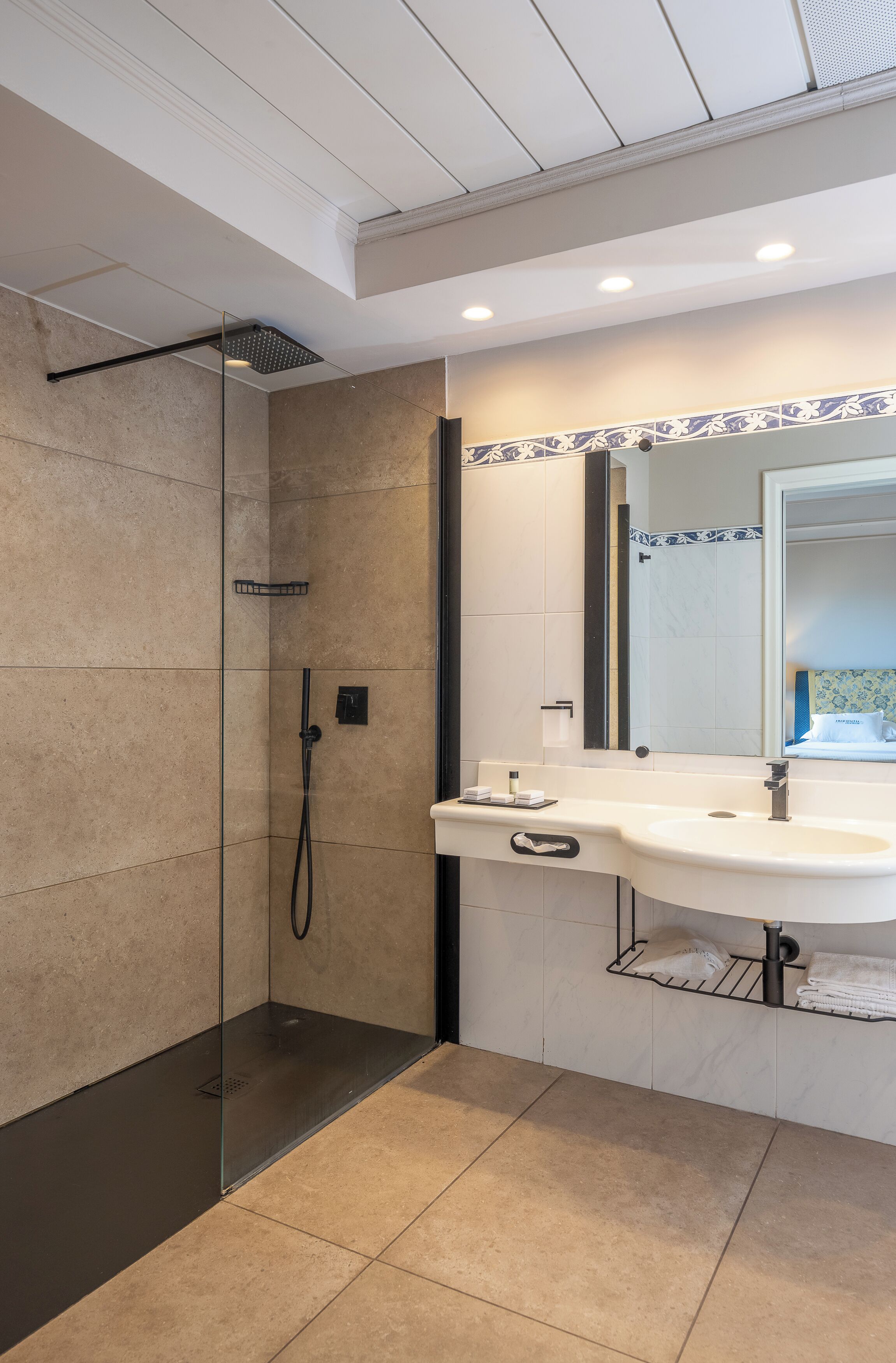 Un bagno moderno con doccia vetro, un lavandino bianco e uno specchio con bordo decorato in piastrelle.