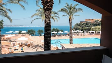 Un área junto a la piscina con sillas de descanso, sombrillas y vista al mar.