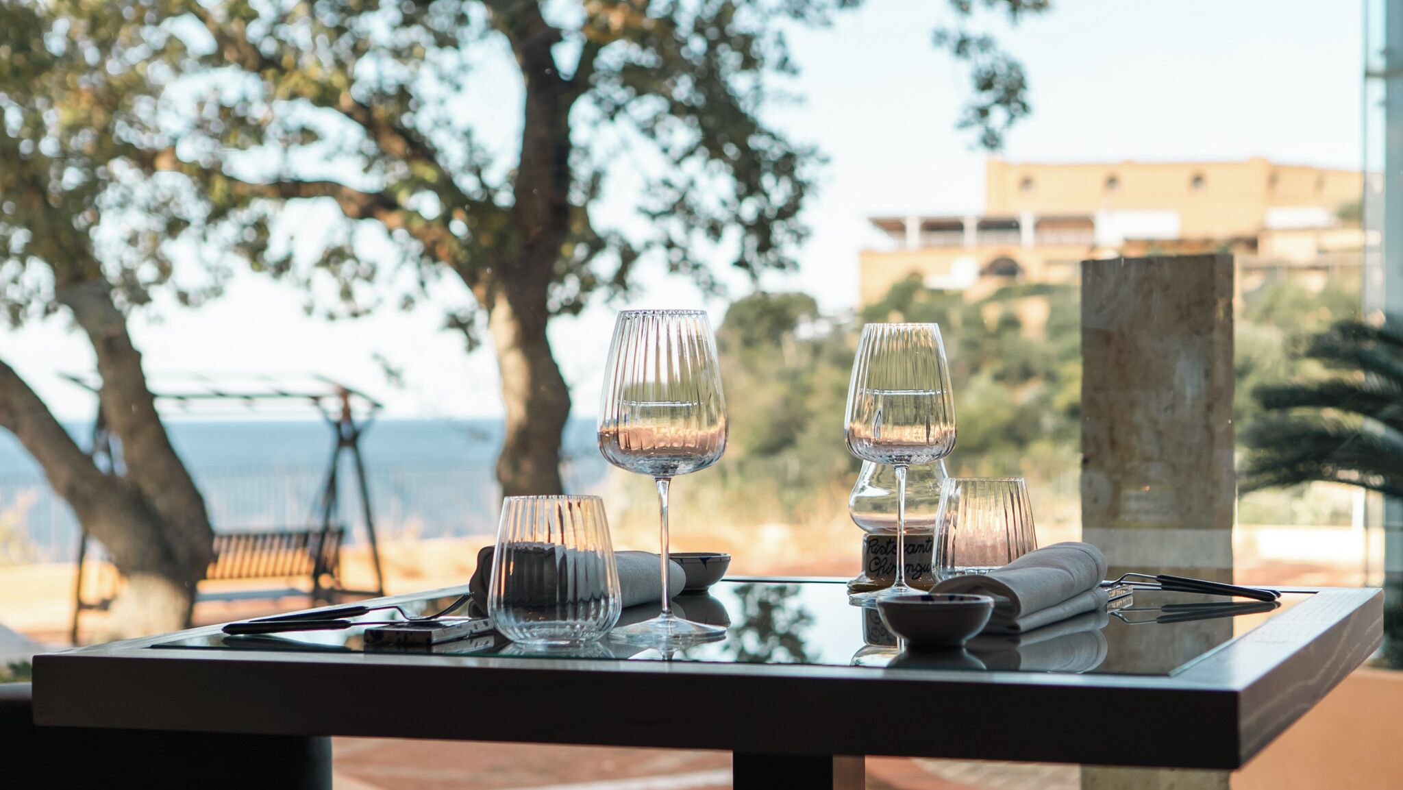 A table set with wine glasses, a bowl, and cutlery, overlooking a scenic view with trees and a building in the background.