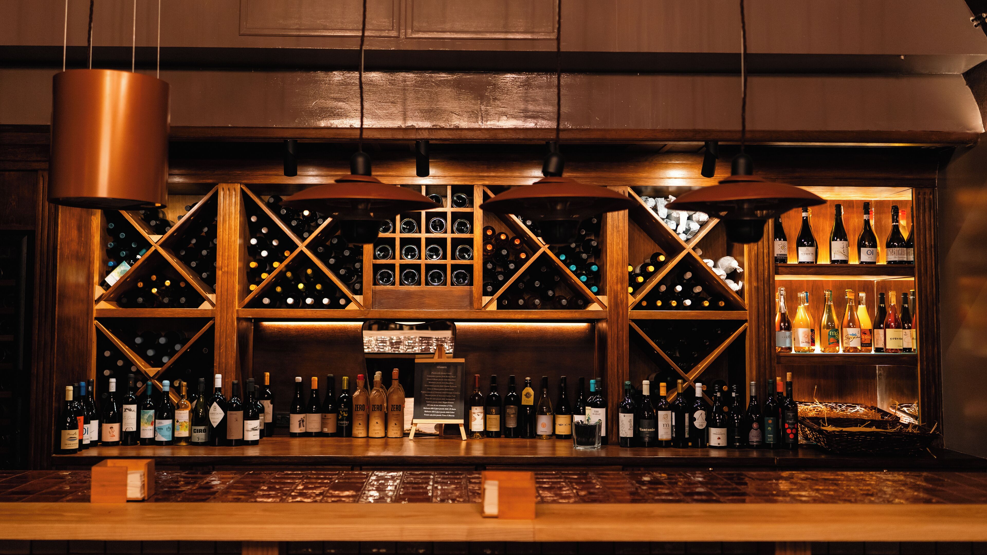 A bar area with wooden shelves and hanging lights, displaying various bottles of wine and spirits.