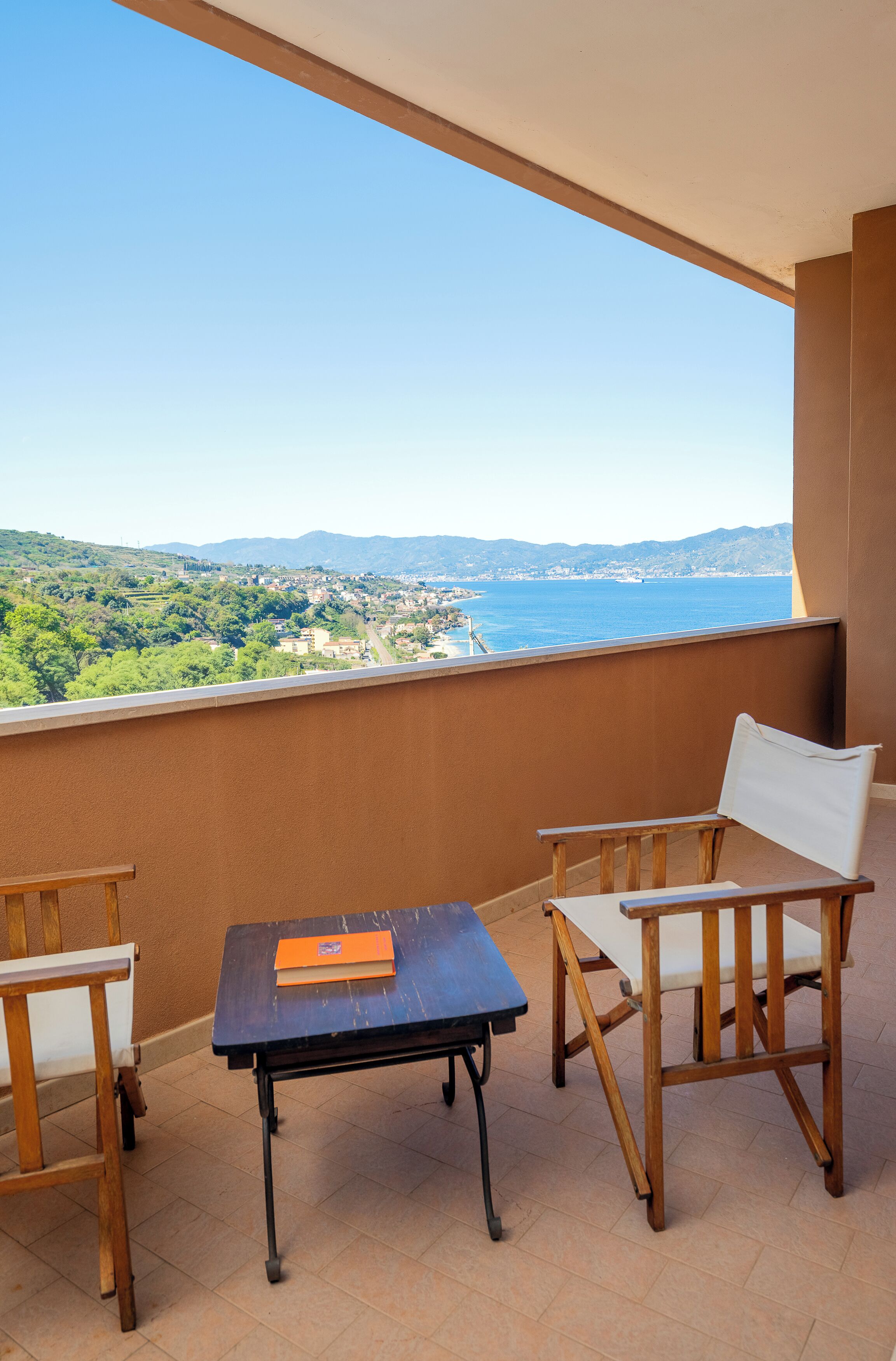 Un balcón con mesa y sillas, con vista a un paisaje costero.