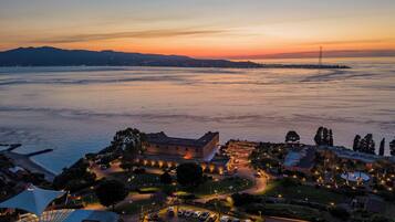 A coastal hotel with a parking area, a large building with a dome, and a view of the sea and distant mountains.