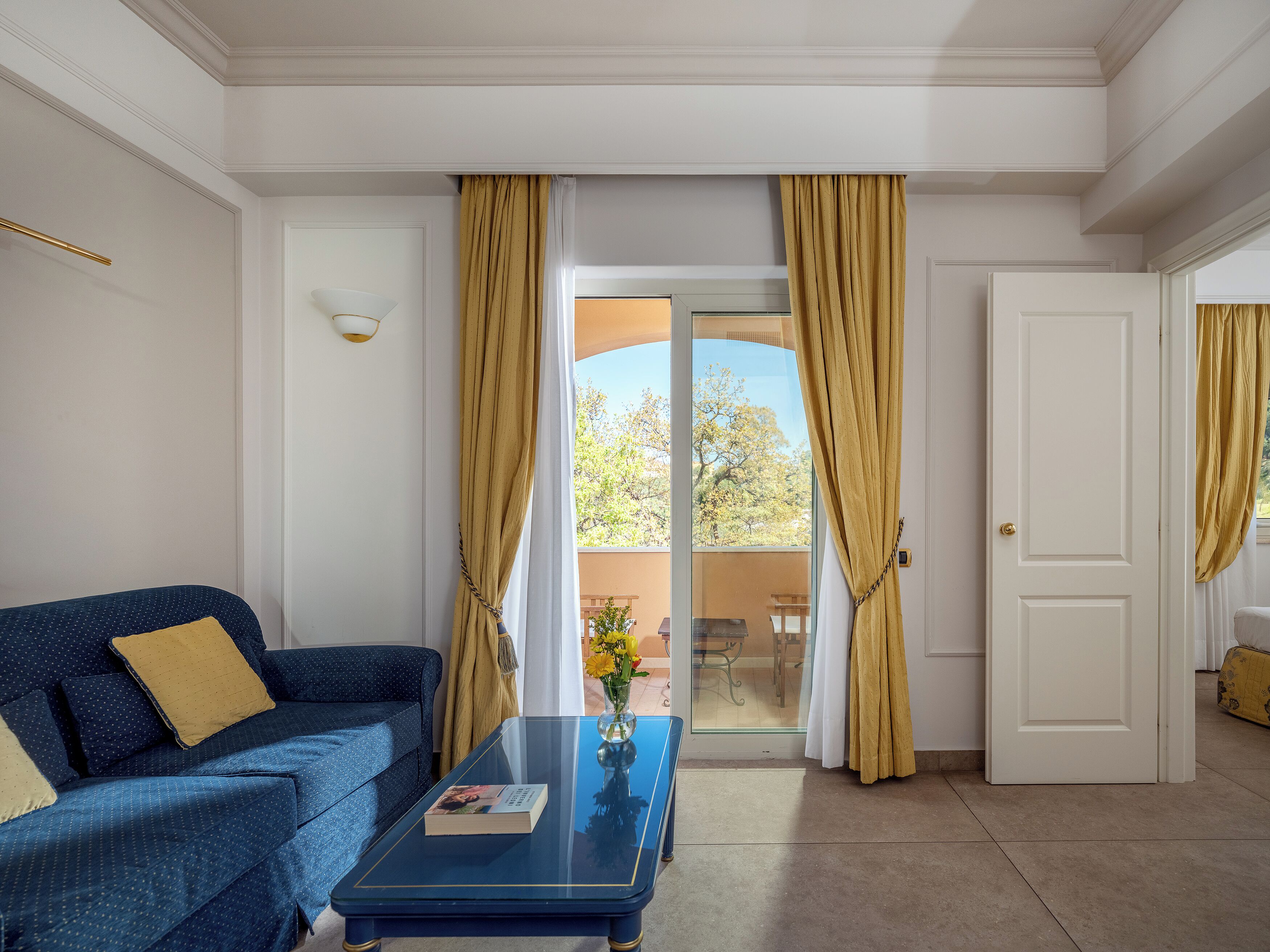 Una habitación con un sofá azul, una mesa de centro de vidrio y una puerta que da a un espacio exterior.