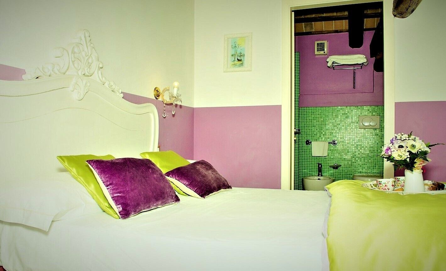 Ein Schlafzimmer mit Bett, Kissen, einem Nachttisch, einer Vase mit Blumen und einem durchgegangenen Tür erkennbaren Badezimmer.