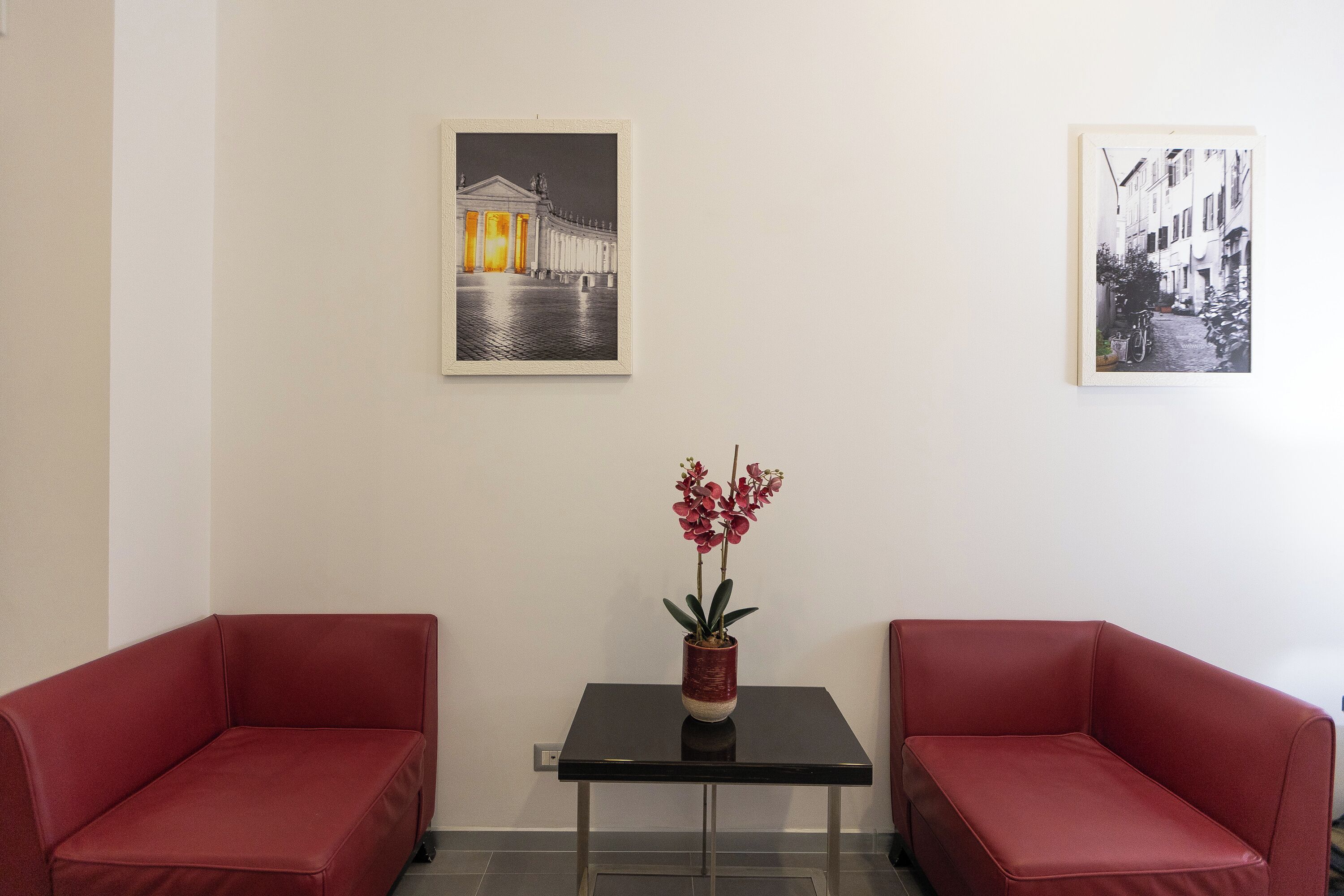 A room with two red sofas, a small table with a potted plant, and two framed pictures on the wall.