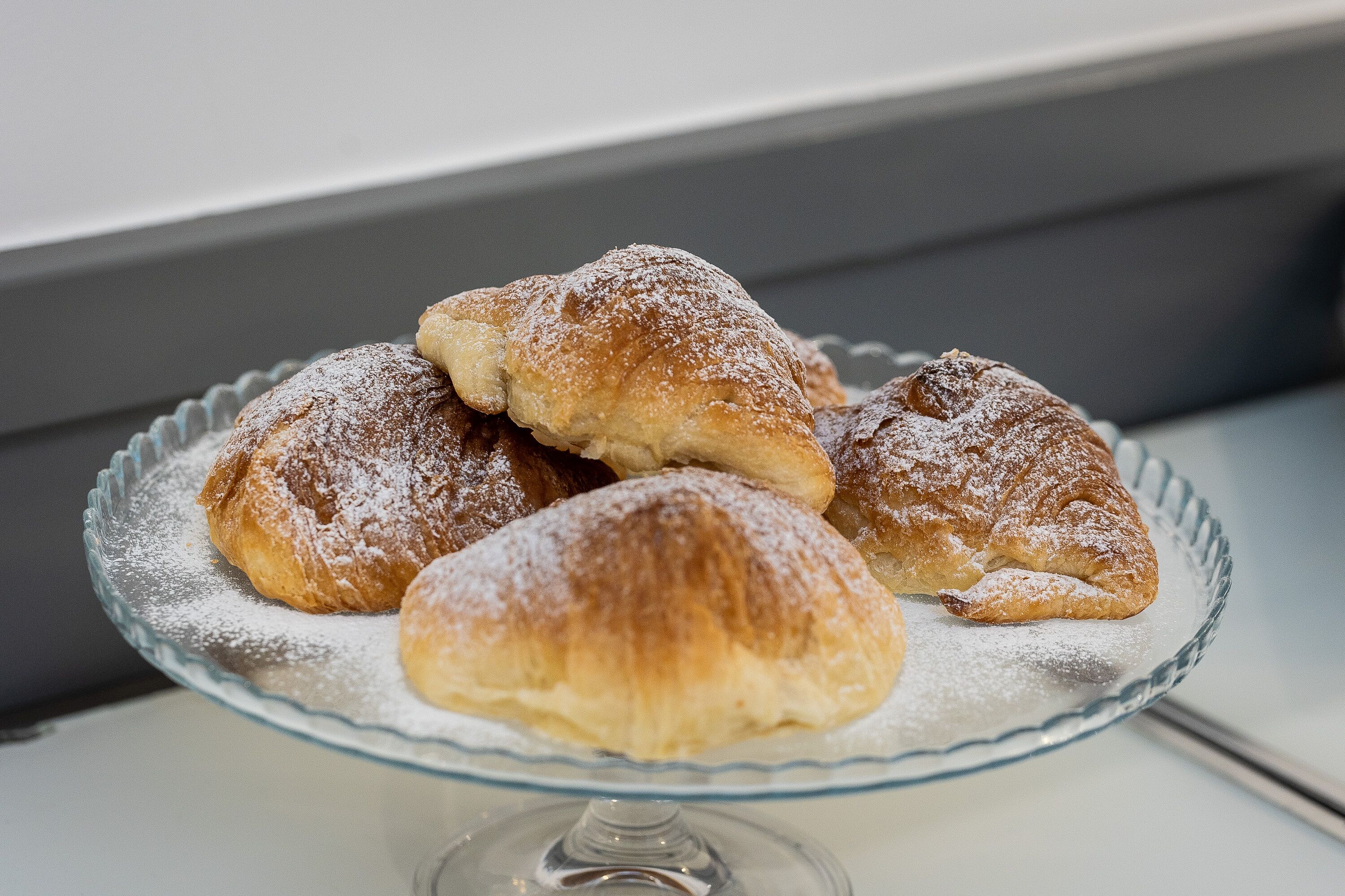 Une assiette en verre contenant trois pâtisseries saupoudrées de sucre glace.