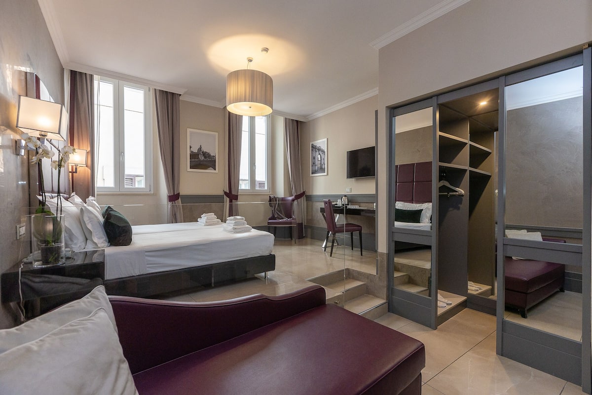 A modern hotel room with a bed, a desk, a chair, and a walk-in closet.