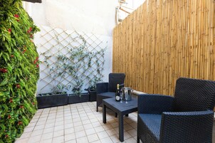 A patio with black wicker furniture, a table with a bottle and glass, and a bamboo fence.