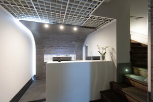 A modern interior with a wooden ceiling, a white reception desk, and a staircase with green steps.