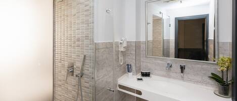 A modern bathroom with a glass-enclosed shower, a white vanity with a large mirror, and a potted orchid on the counter.