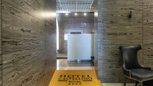 A hotel reception area with a reception desk, a black leather chair, and a wooden textured wall. - Hotel Castellino Roma (Rome)