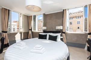 Hotelkamer met een groot bed, twee bedlampen, uitzicht op de stad door grote ramen en een moderne kroonluchter.