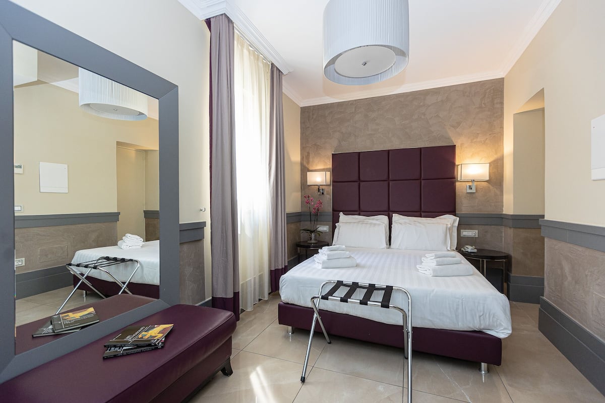 A modern hotel room with a large bed, bedside tables, a mirror, and a seating area.