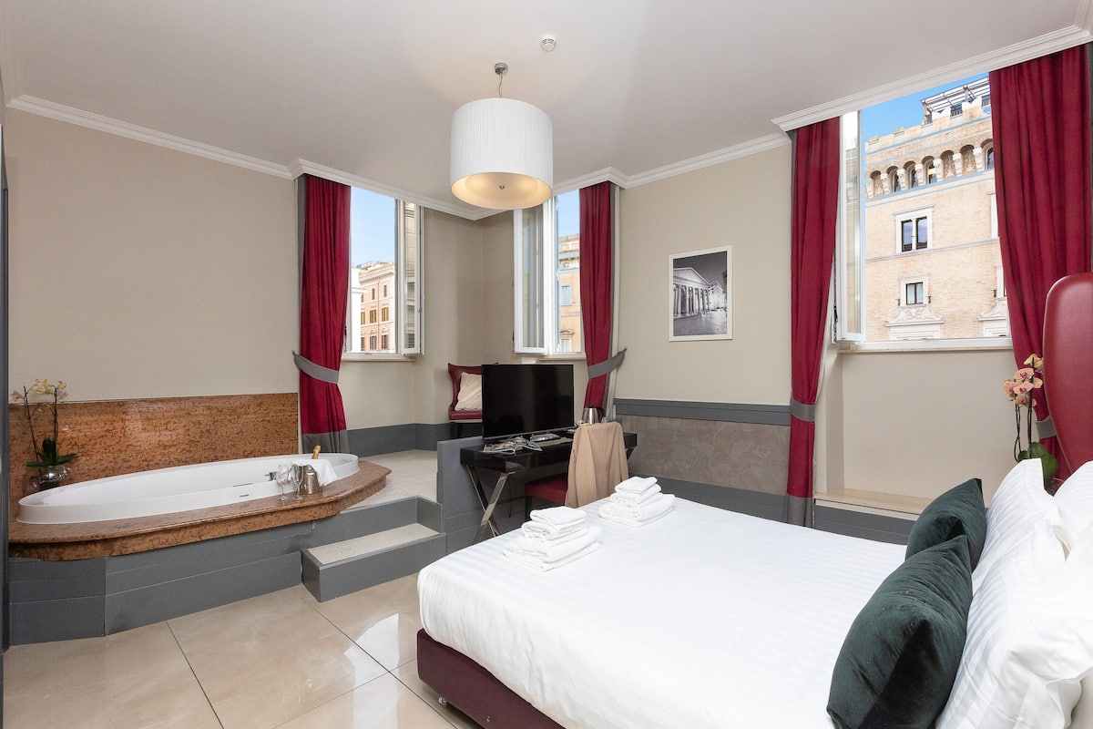 A hotel room with a large bed, a separate bathroom with a bathtub, a desk, and a television.