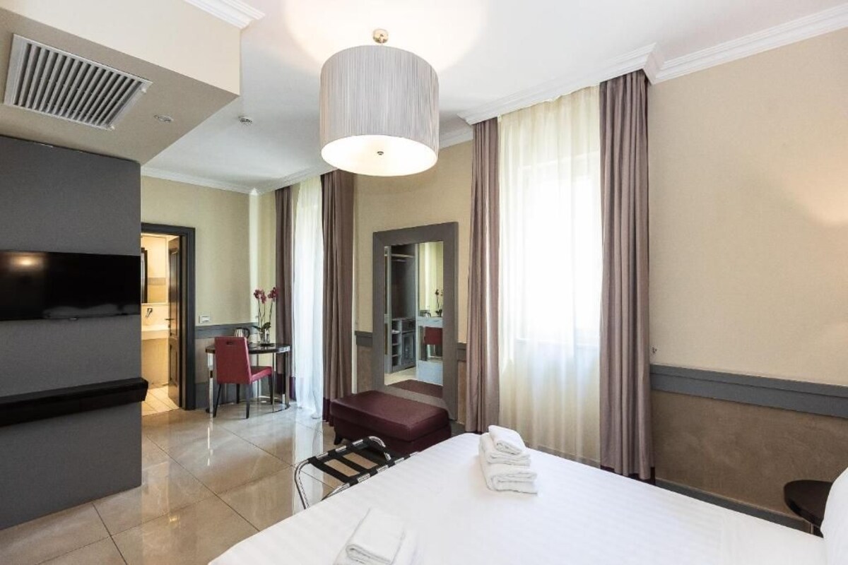 A hotel room with a bed, a desk, a chair, a television, and a bathroom visible through an open door.