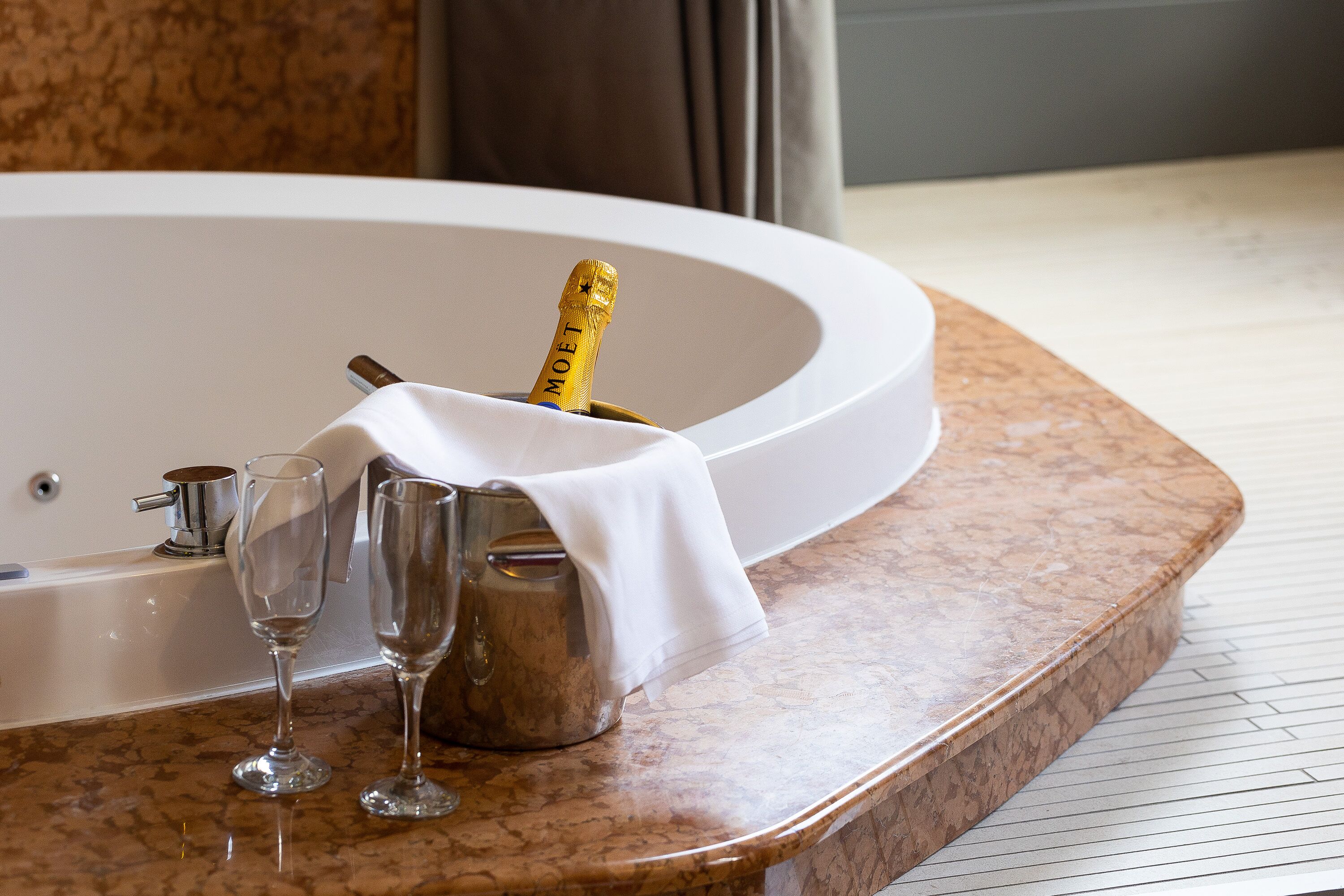 A bathroom with a marble countertop, a bathtub, and two champagne flutes.