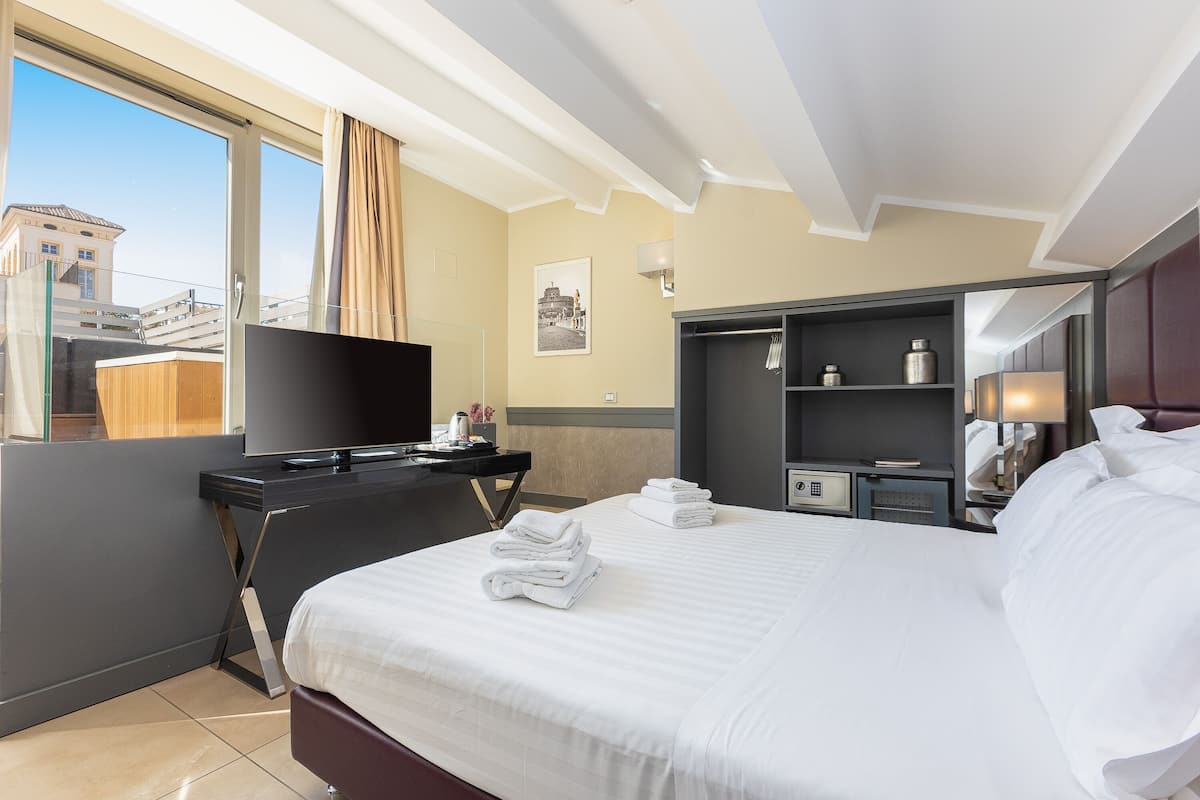 A hotel room with a bed, a desk, a TV, and a view of the city.