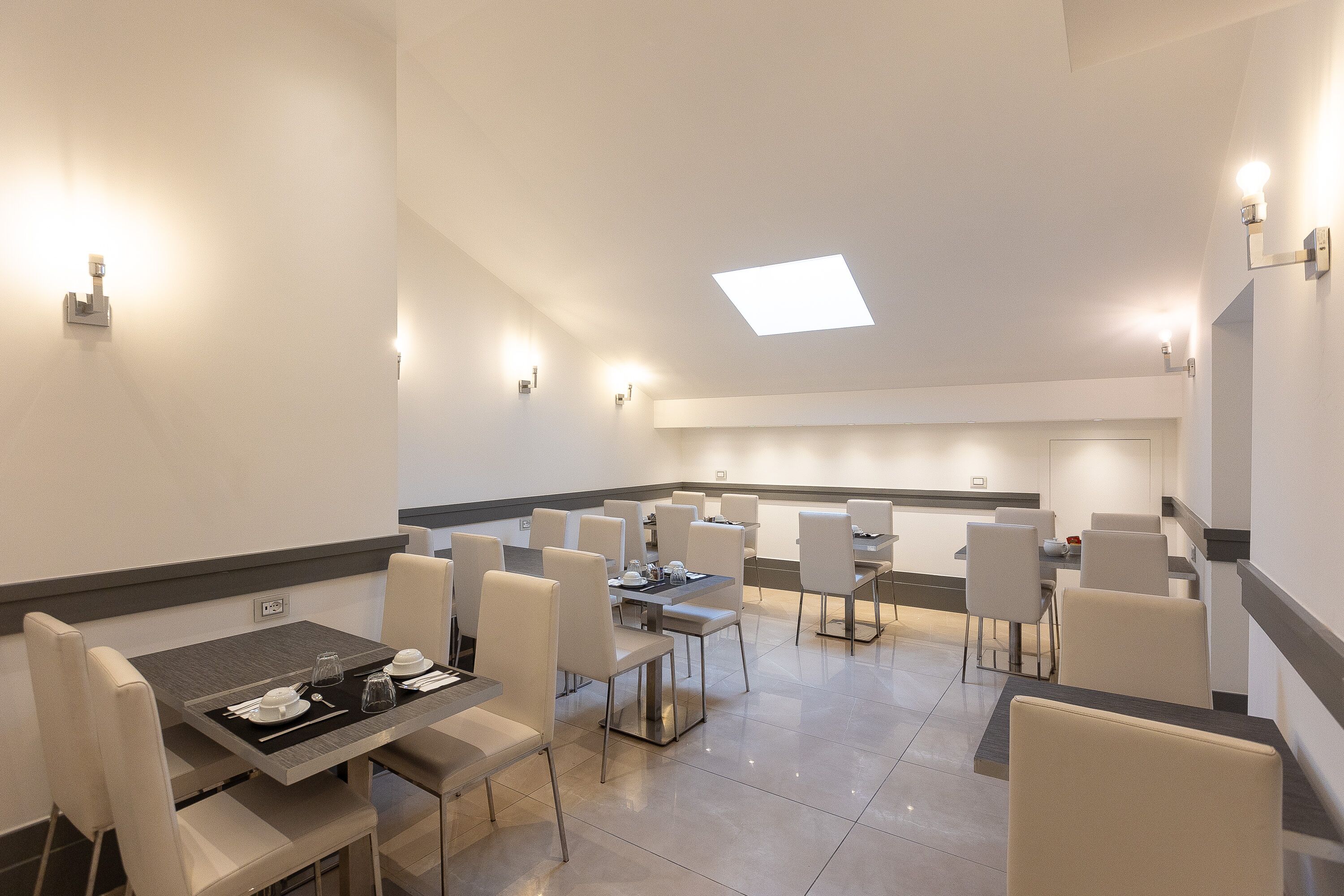 Un'area pranzo moderna con diversi tavoli e sedie, un'isola centrale e un lucernario.