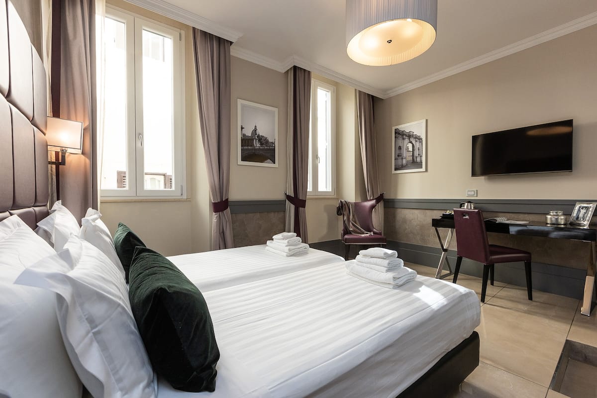 A hotel room with a large bed, a desk, a chair, and a TV.
