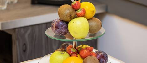 A three-tiered fruit stand with apples, kiwis, strawberries, and an orange on a glass table.