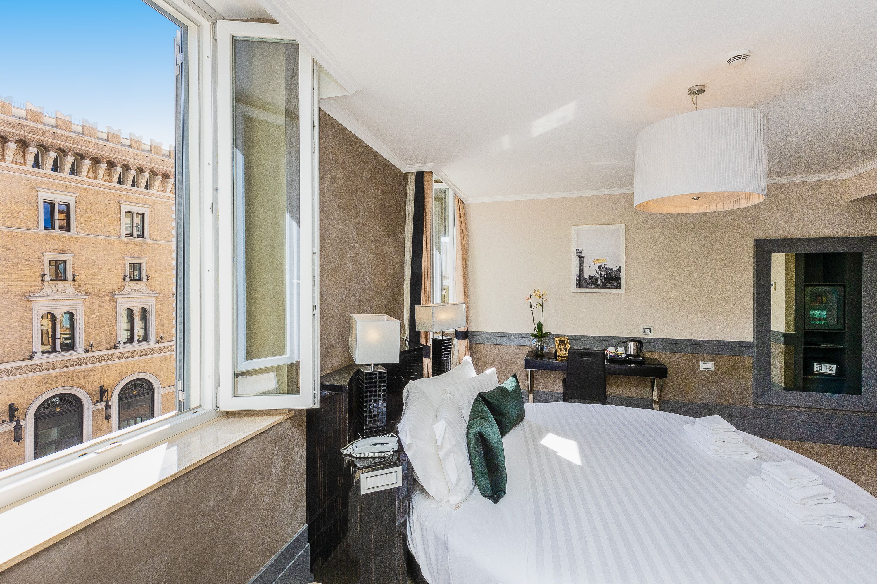Habitación de hotel con una cama grande, una mesita de noche, un escritorio y ventana con vistas a un edificio histórico.