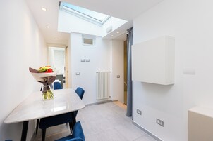 A modern kitchen with a skylight, white cabinets, and a dining area with blue chairs and a vase of flowers.