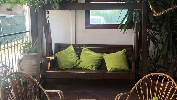 A patio area with a wooden swing seat, two wicker chairs, and a small table with a basket.