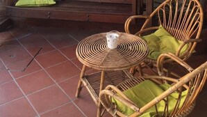 A wooden bench with a green cushion, a wicker chair with a green cushion, and a small table with a white bucket.