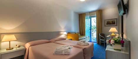 A hotel room with two beds, a desk, a chair, a TV mounted on the wall, and a window with curtains.