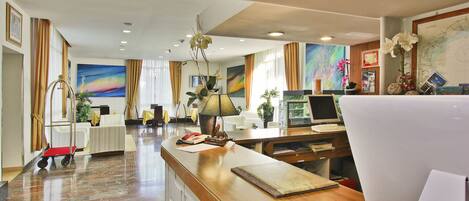 A hotel reception area with a wooden reception desk, a computer, and a map on the wall.