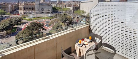 Ein Balkon mit Tisch für zwei Personen, mit Blick auf eine Stadtlandschaft, die historische Gebäude und einen Brunnen zeigt.