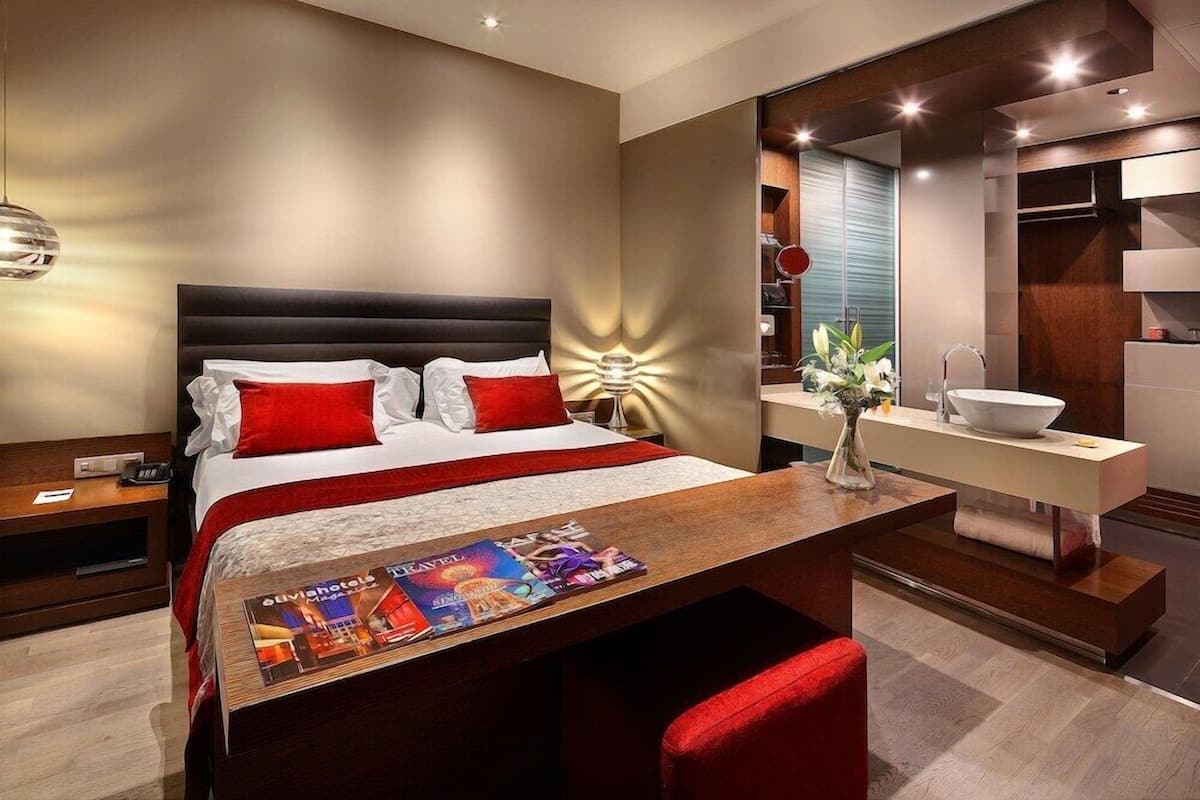 A modern hotel room with a large bed, bedside table, and a desk with a magazine.