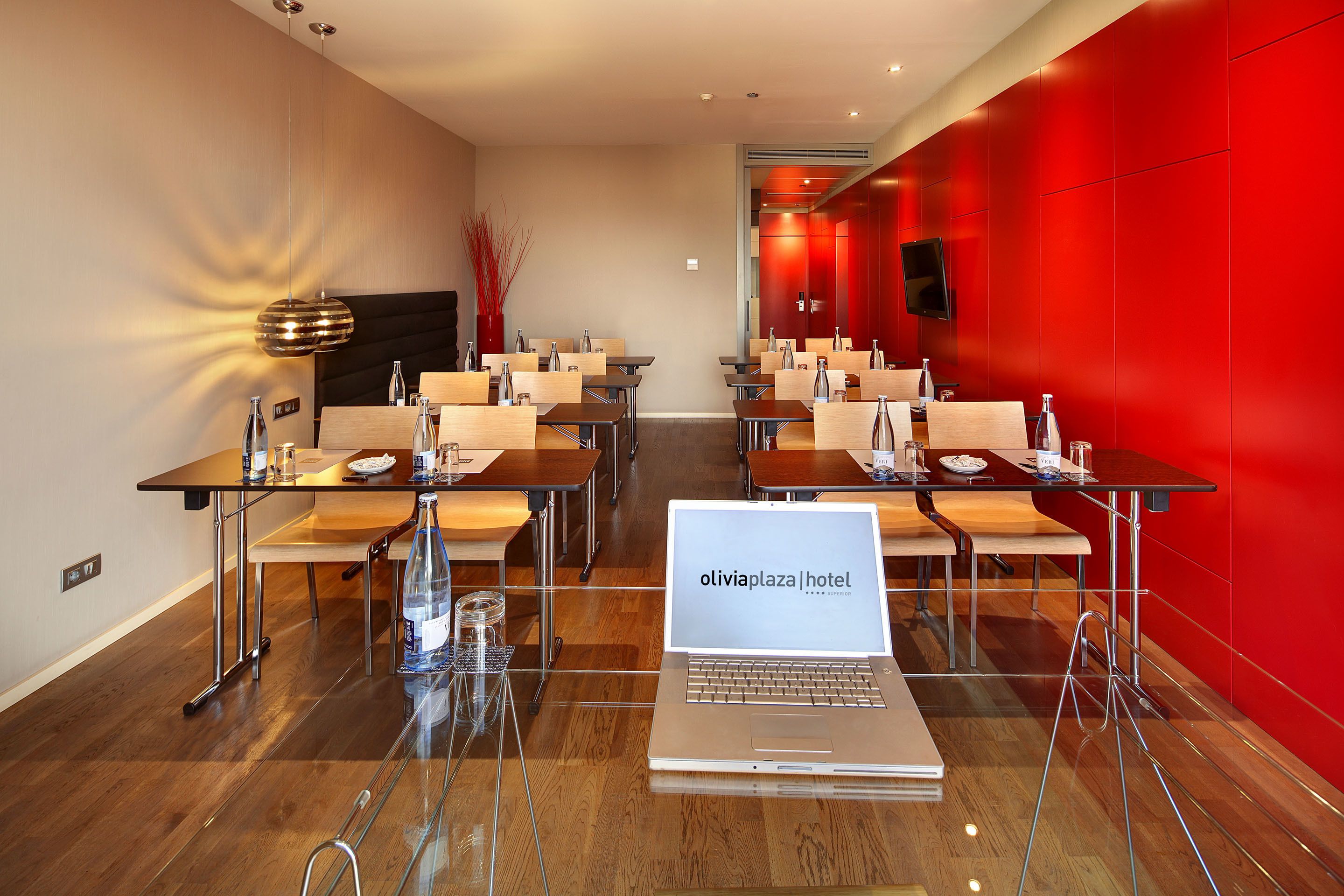 A modern hotel conference room with tables, chairs, and a laptop displaying the hotel name.
