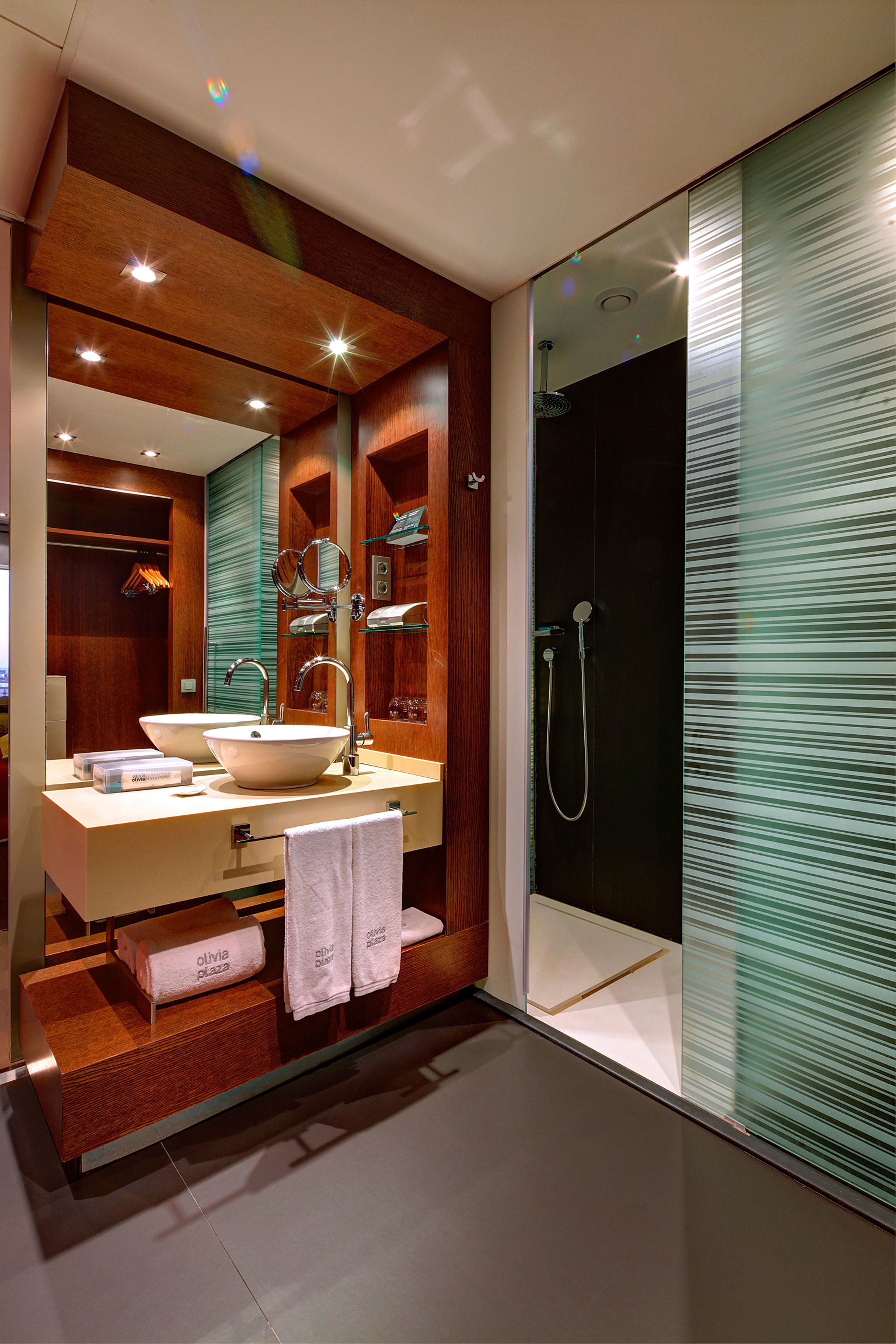 A modern bathroom with a large mirror, two sinks, a shower, and a glass partition.