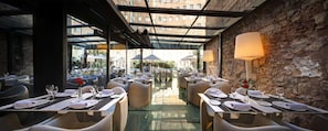 Un restaurant avec des tables dressées, un mur en pierre et un plafond en verre.