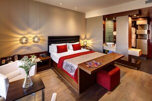 A modern hotel room with a large bed, bedside tables, a wooden desk, and a built-in wardrobe.