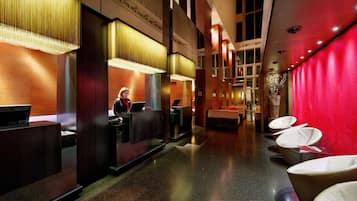 A hotel lobby with a reception desk, a seating area with chairs, and a red accent wall.