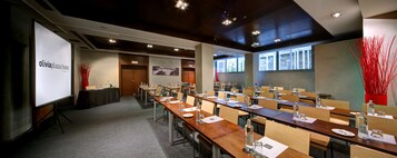 Un salón de conferencias con varias mesas, sillas y una pantalla de proyección.