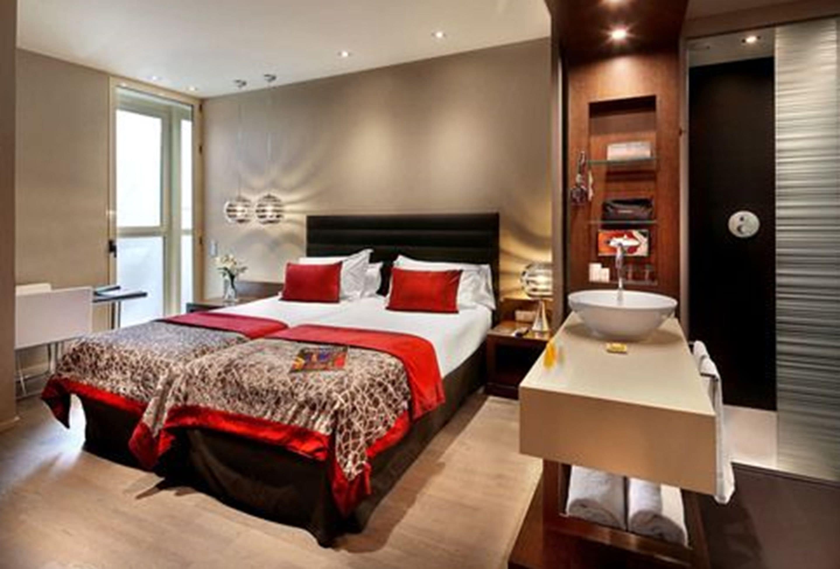 A modern hotel room with a large bed, a bedside table with a lamp, a bathroom with a sink and mirror, and a view of the city.