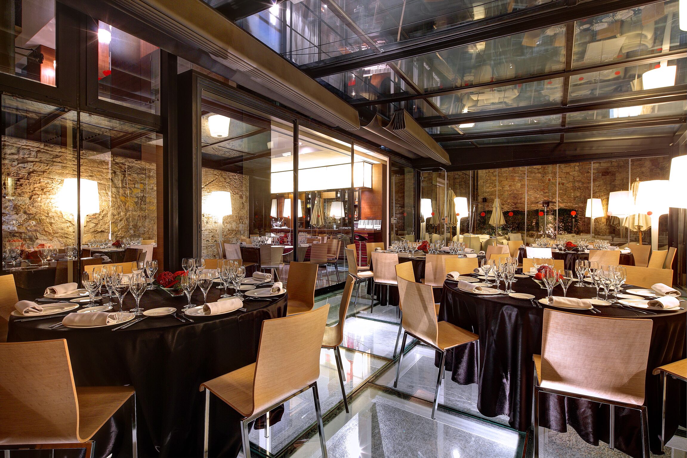 Un restaurante con varias mesas dispuestas para comer, divisiones de vidrio y una decoración interior moderna.