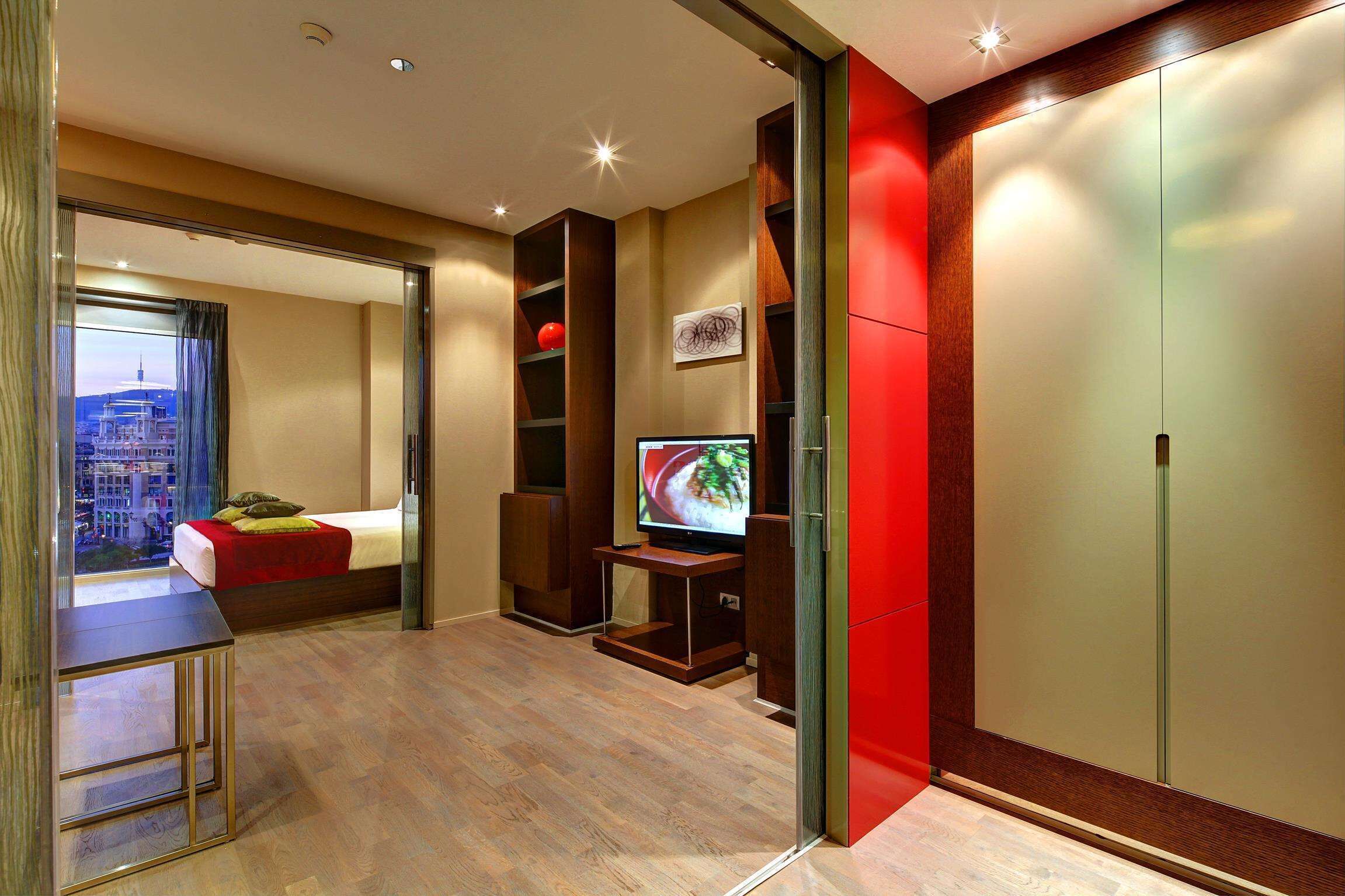 A modern hotel room with a bed, a TV, a desk, and a city view.