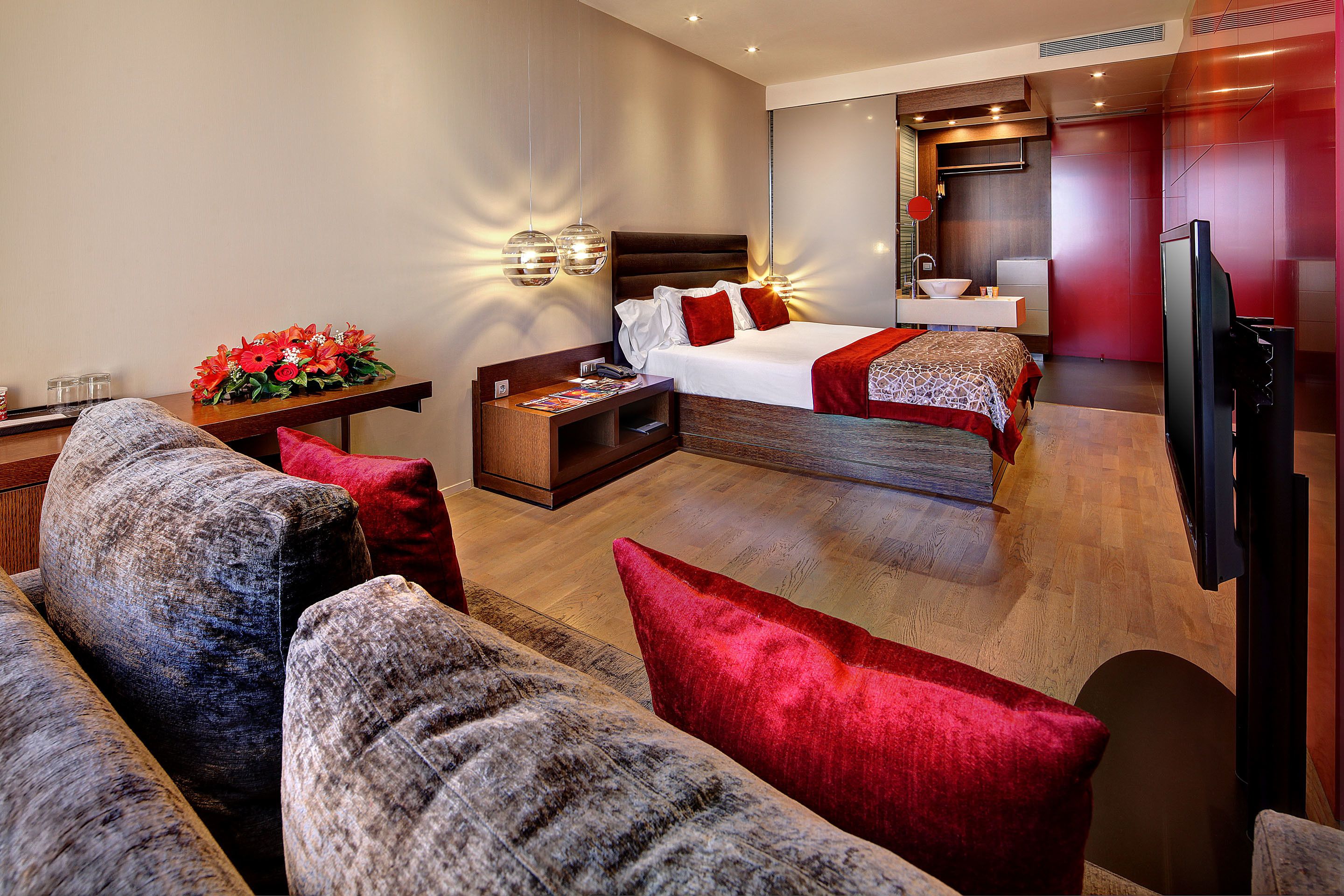 Una habitación de hotel moderna con una cama grande, un sofá, un televisor y una pequeña mesa con un jarrón de flores.