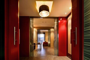 A modern interior with a red accent wall, a glass door leading to a bedroom, and a city view.