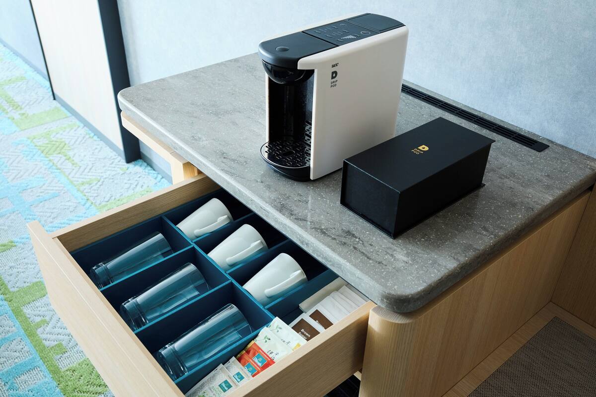 Une machine à café, un tiroir contenant des tasses à café et une boîte posée sur un plan de travail.