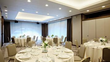 Un salón de conferencias con mesas redondas, sillas y un amplio ventanal con cortinas.