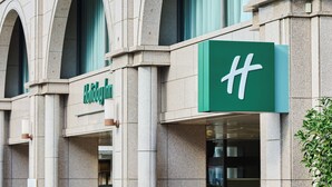 Ein Holiday Inn Schild an einer Gebäudefassade mit rundbogigen Fenstern und einer grünen Beschilderung.