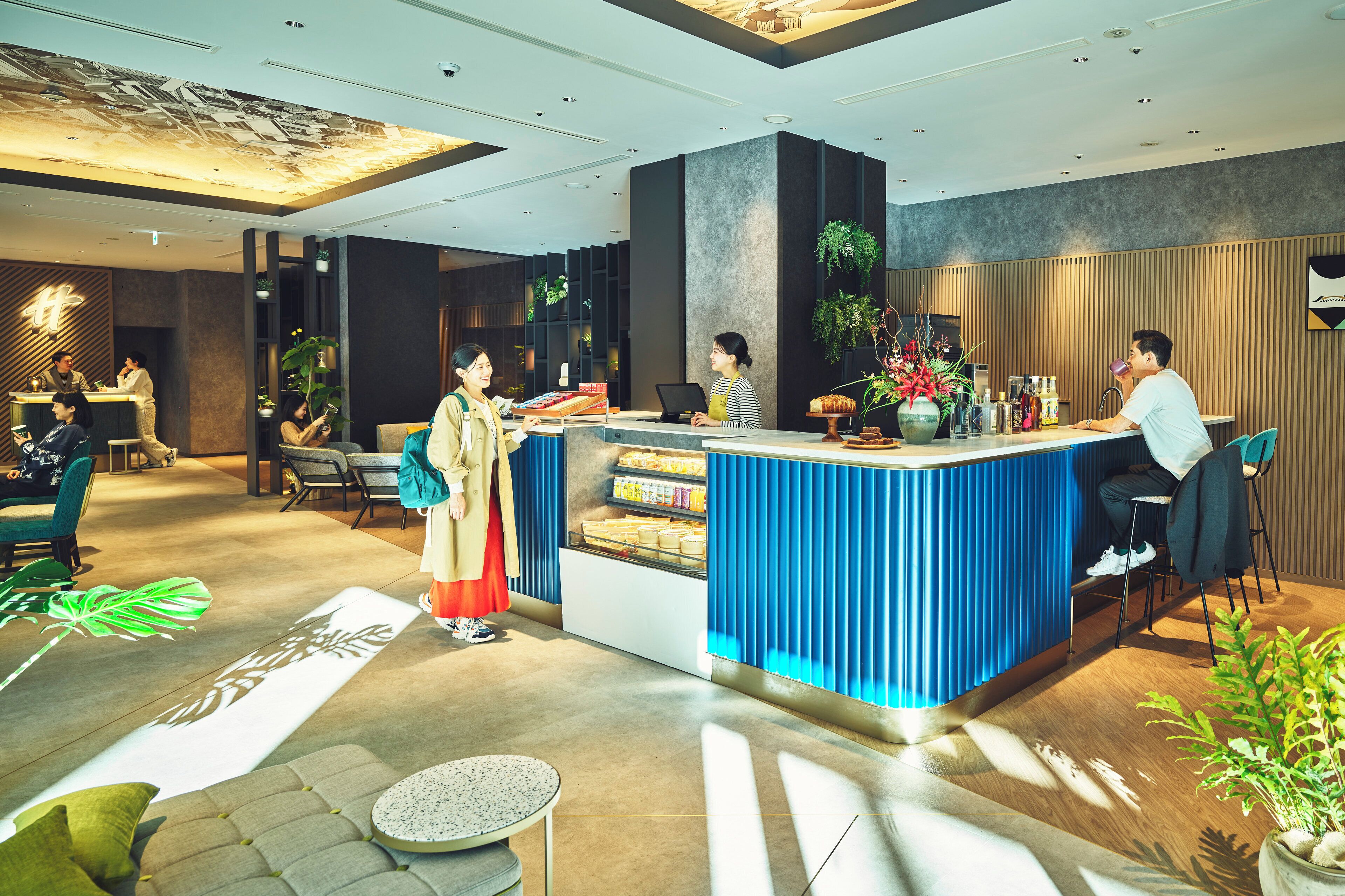 A modern hotel lobby with a reception desk, seating area, and decorative plants.